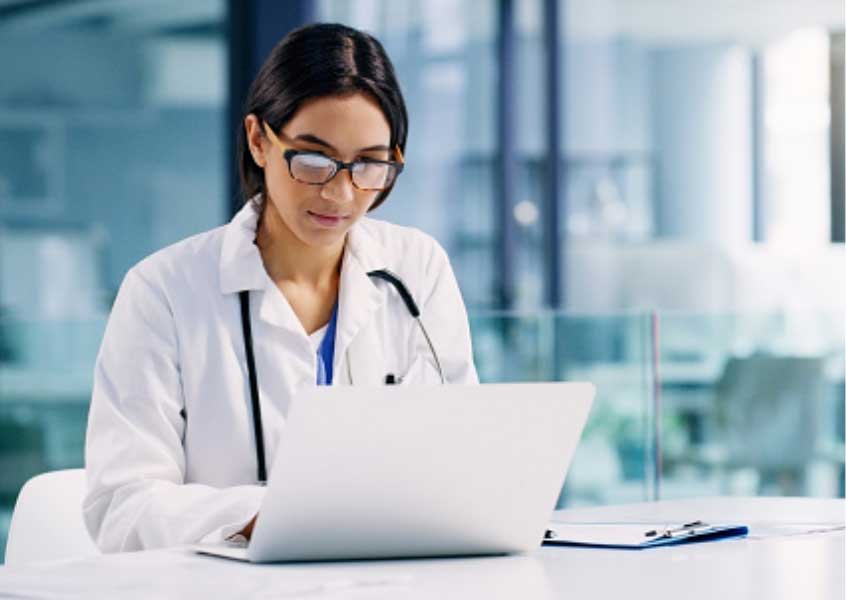A doctor works on a computer reviewing benefits